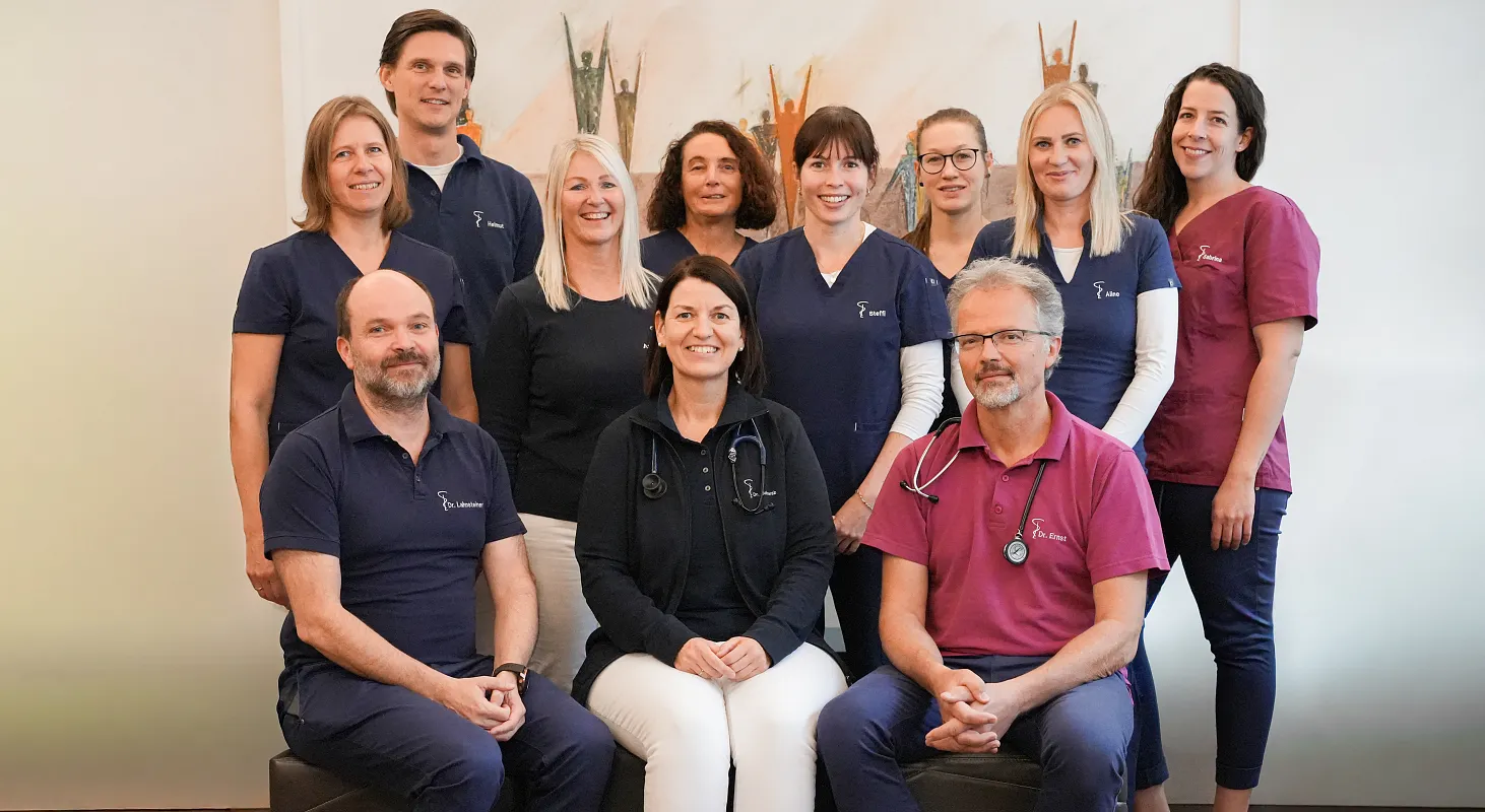 Eine Gruppe von elf Personen, bestehend aus Männern und Frauen, posiert in zwei Reihen. Alle tragen ärztliche Berufskleidung in verschiedenen Farben.