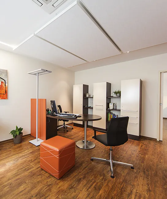 Ein modernes Büro mit Holzboden, einem Schreibtisch, einem runden Tisch, mehreren Stühlen und Regalen. An der Wand hängt ein abstraktes Gemälde.