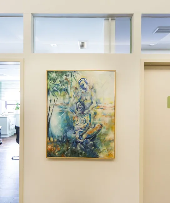 Flur in einer Arztpraxis mit einem Gemälde an der Wand und einer Tür mit der Aufschrift "Arzt 2". Links ist ein Behandlungsraum mit Liege zu sehen.